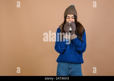 Une fille dans un chapeau et des gants portant un mug. Isolé sur fond brun Banque D'Images