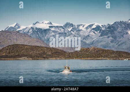 Paysage arctique du Groenland lors d'une journée ensoleillée en été. Petit bateau de pêche dans les eaux ouvertes. Vue magnifique sur les montagnes avec les sommets enneigés et les Glaciers Banque D'Images