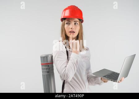 Femme architecte se tient avec un tube derrière son dos tenant l'ordinateur portable et regarder perdu dans la pensée Banque D'Images