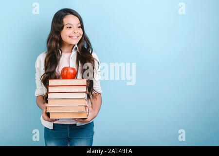 Portrait de jeune fille souriante tenant pile de livres avec pomme dessus. Retour à l'école. - Copyspace Banque D'Images