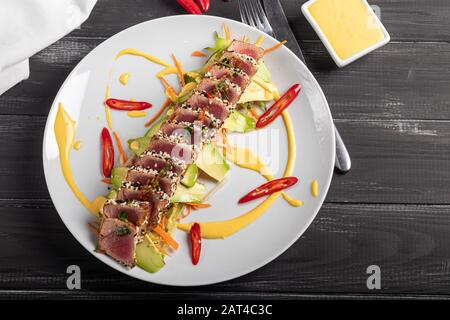 Cuisine japonaise. Tatataki avec thon. Poisson frit avec graines de sésame et sauce soja, wasabi, citron vert. Sur un oreiller de légumes. Avocats, bandes de piment Banque D'Images