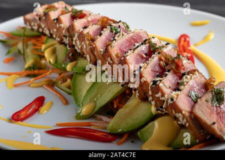 Cuisine japonaise. Tatataki avec thon. Poisson frit avec graines de sésame et sauce soja, wasabi, citron vert. Sur un oreiller de légumes. Avocats, bandes de piment Banque D'Images