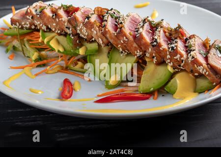 Cuisine japonaise. Tatataki avec thon. Poisson frit avec graines de sésame et sauce soja, wasabi, citron vert. Sur un oreiller de légumes. Avocats, bandes de piment Banque D'Images