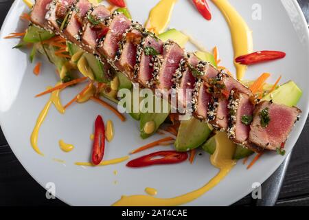 Cuisine japonaise. Tatataki avec thon. Poisson frit avec graines de sésame et sauce soja, wasabi, citron vert. Sur un oreiller de légumes. Avocats, bandes de piment Banque D'Images