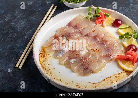 dorado léger salé avec tournesol dans de l'huile de truffe. À côté de tranches de citron, de chaux, de raisins, de gingembre mariné. Sur le côté de la plaque se trouvent des baguettes. Activé Banque D'Images