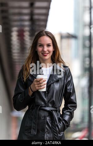 Jeune femme tenant une tasse à café en papier à l'extérieur et souriant. Faible profondeur de champ. Prise de vue moyenne. Banque D'Images