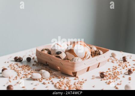 Jour de Pâques. Œufs de Pâques dorés dans un panier en bois, grains de blé, bonbons au chocolat sur une table blanche. Félicitations Banque D'Images