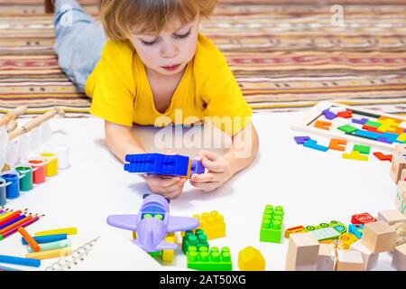 Jeu de garçon Prescool avec des blocs, avion et voitures. Jouets éducatifs pour enfants d'âge préscolaire et de jardin d'enfants, à partir du sol sur papier. Enfant à la maison ou en garderie. Banque D'Images