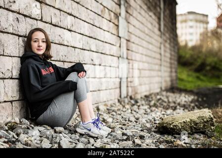 Portrait d'une jeune fille universitaire sportive de 17 ans posant contre un mur rugueux sous un pont à Molenbeek, Bruxelles, Belgique Banque D'Images