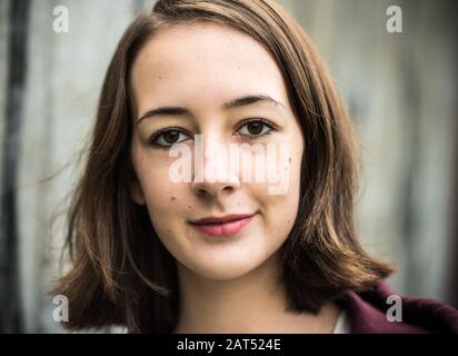 Headshot d'une jeune fille de 17 ans d'université avec un accrochage posant contre un mur rugueux Banque D'Images