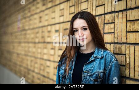 Headshot d'une jolie jeune fille d'université blanche de 18 ans avec de gros yeux bruns se posant contre un mur en bokeh Banque D'Images