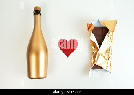Bouteille de champagne doré et bar au chocolat en wrapper or et coeur pailleté rouge sur fond blanc. Ensemble festif. Vue de dessus Banque D'Images