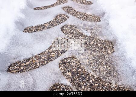 Traces d'un pneu de tracteur sur de l'asphalte neigeux sur une route en hiver. Banque D'Images