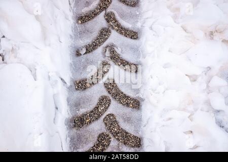 Détail des traces d'une roue sur l'asphalte enneigé, vu d'en haut. Banque D'Images