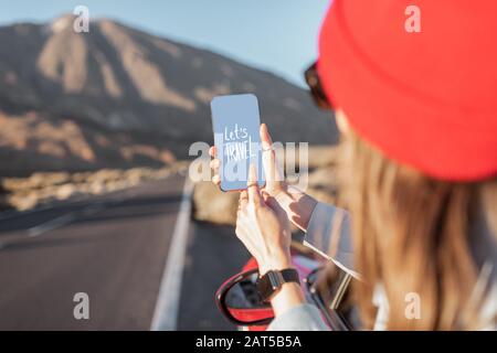 Femme voyageant en voiture sur la vallée volcanique, se penchant hors de la fenêtre de voiture, tenant smartphone avec texte appelant pour voyager Banque D'Images