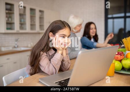 Fille regardant un ordinateur portable à une table dans la cuisine. Banque D'Images