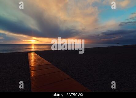 Plage vide de Calahonda sur la Costa del sol, Andalousie. Des poutres lumineuses au lever du soleil se reflètent dans la promenade en bois, ciel nuageux et moelleux, Espagne Banque D'Images