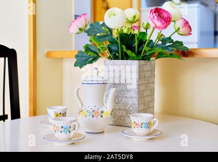 Mignonne théière et tasses avec motif fleuri sur table blanche belle buttercup persan ranunculus bouquet rose blanc brillant couleurs dans vase pas de personnes Banque D'Images