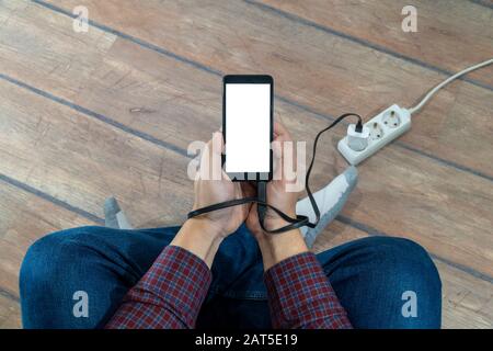 Concept de problèmes modernes. Homme tenant un téléphone mobile avec écran vide connecté à un coupleur électrique. Mains attachées avec le câble du chargeur. Banque D'Images