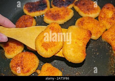 Une main avec une spatule en bois retourne sur la friture des pépites de poulet dans une poêle à frire. Gros plan Banque D'Images