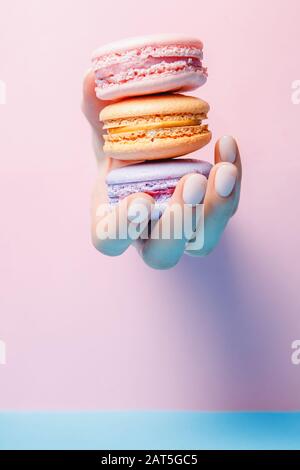 Belle fille main avec manicure à la mode prenant des macarons de couleur sur fond rose et bleu Banque D'Images