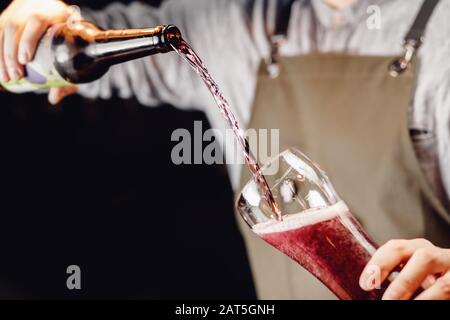 Le Barman verse de la bière à la cerise aux bleuets en verre, fond sombre Banque D'Images