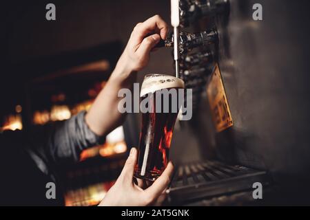 Les barman boivent de la bière artisanale à partir du robinet en verre, fond sombre Banque D'Images