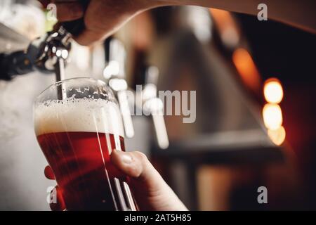 Les barman boivent de la bière artisanale à partir du robinet en verre, fond sombre Banque D'Images