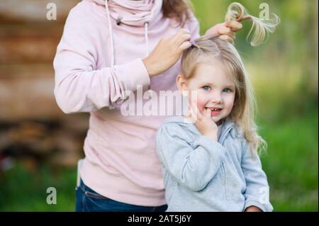 Portrait d'une jeune fille souriante dont la mère pleure un tresse lors d'une soirée d'été, gros plan Banque D'Images