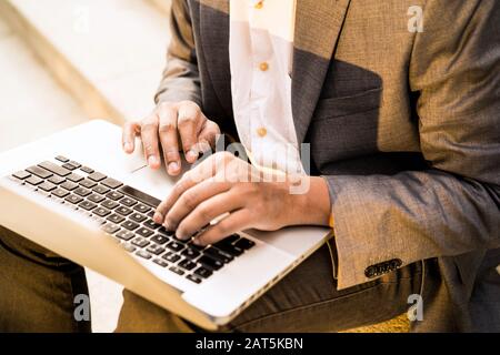Jeune homme de course mixte est assis avec un ordinateur portable et la dactylographie Banque D'Images