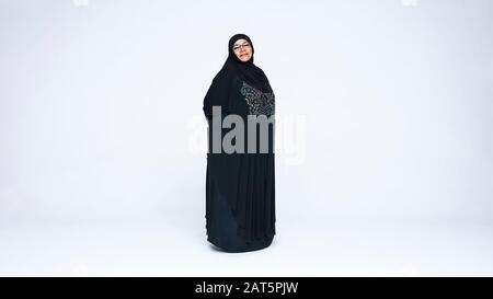 Femme islamique en burqa debout isolée sur fond blanc. Femme islamique souriante regardant l'appareil photo. Banque D'Images