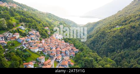Vue sur le village italien de montagne, Garzeno. Vue à grand angle des maisons avec des toits rouges surmontant des arbres sur le sommet de la montagne en été. Banque D'Images
