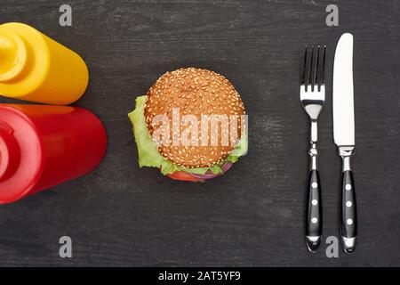 vue de dessus de délicieux hamburger frais près des couverts, du ketchup et de la moutarde sur une table en bois noir Banque D'Images