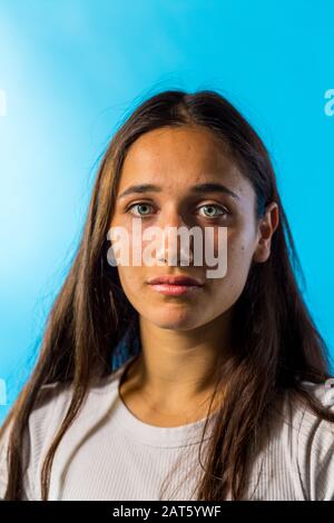 Photo de beauté d'une femme tannée sur peau avec des yeux de couleur claire derrière fond bleu. Gros plan moyen. Banque D'Images