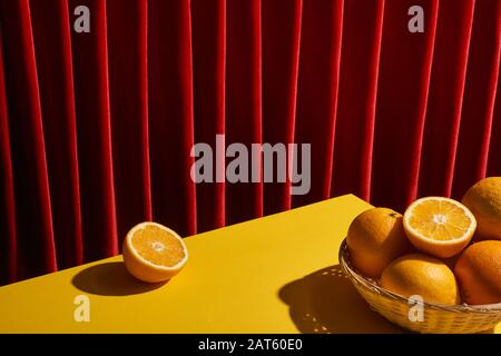 classique toujours la vie avec des oranges dans le panier en osier sur la table jaune près du rideau rouge Banque D'Images