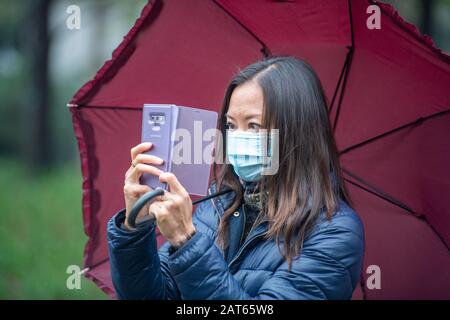 Shanghai, Chine, 26 janvier 2020, une femme portant un masque prend une photo avec son téléphone portable tout en tenant un parapluie Banque D'Images