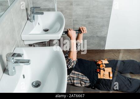 vue courte de l'installateur tenant la pince à joint coulissant près du tuyau tout en reposant sur le sol dans la salle de bains Banque D'Images