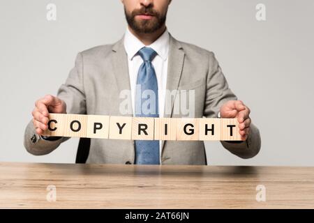 vue rognée d'un homme d'affaires tenant des cubes de bois avec mot copyright isolé sur gris Banque D'Images