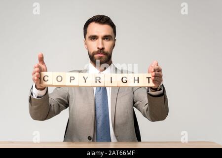 homme d'affaires confiant tenant des cubes de bois avec des lettres de copyright isolées sur gris Banque D'Images