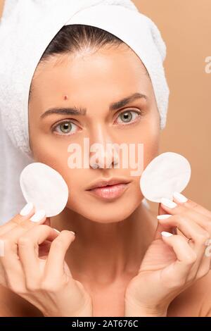 jeune femme avec un pompon sur le visage tenant des tampons de coton isolés sur le beige Banque D'Images