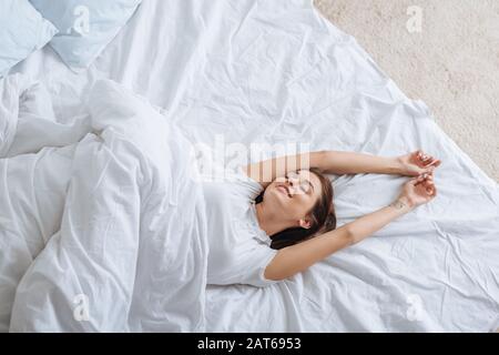 vue de dessus de la jeune femme positive avec des yeux fermés reposant dans le lit Banque D'Images