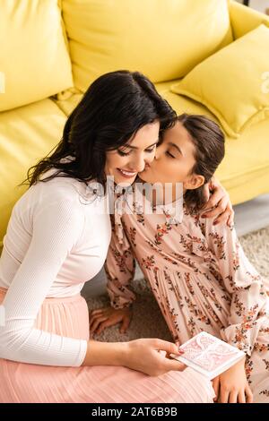 heureuse femme tenant la carte de fête des mères tout en adorable fille la baiser Banque D'Images