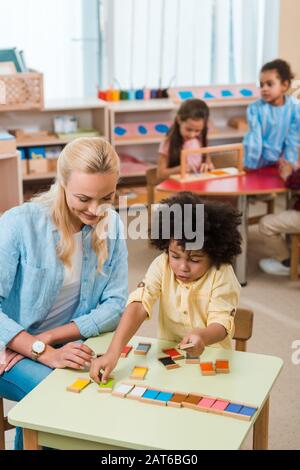 Foyer sélectif de jeu d'enfant en souriant professeur avec des enfants en arrière-plan à l'école de montessori Banque D'Images