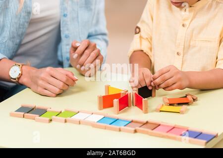 Vue rognée des enfants et des enseignants jouant à un jeu éducatif à la table pendant la leçon de la classe montessori Banque D'Images