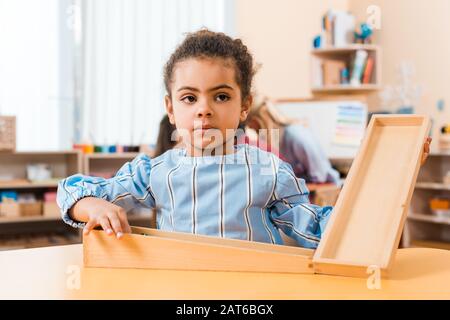 Foyer sélectif de l'enfant africain américain avec jeu en bois et professeur avec des enfants en arrière-plan à l'école de montessori Banque D'Images