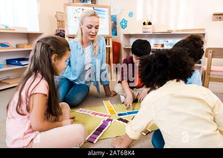 Enfants jouant au jeu éducatif par professeur sur le sol en classe montessori Banque D'Images