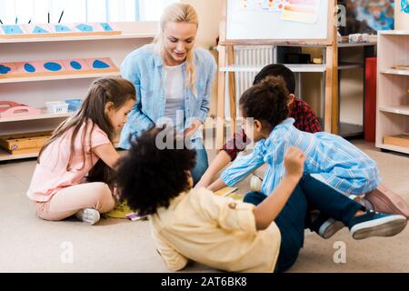 Foyer sélectif de l'enseignant et des enfants jouant au jeu sur le sol à l'école de montessori Banque D'Images