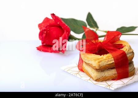 Cookies en forme de coeur attachés avec un noeud rouge et rose rouge isolé sur fond blanc. Concept de Saint-Valentin ou d'anniversaire. Banque D'Images