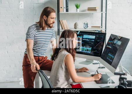 éditeur d'art barbu près d'un collègue attrayant travaillant en studio Banque D'Images