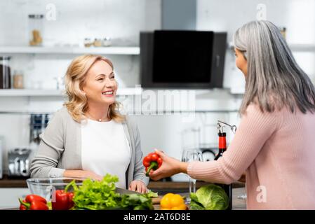 une femme souriante cuisinant et parlant avec son ami avec du poivron Banque D'Images